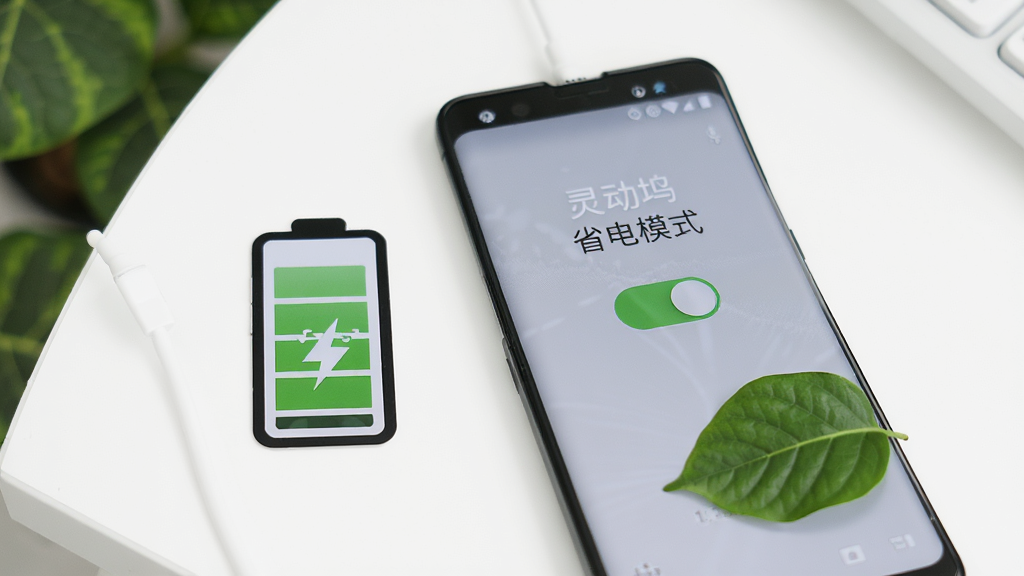 一张展示灵动坞轻量省电特性的图片,画面中一部安卓手机旁边放置着一个电池图标和一片绿叶,手机屏幕显示灵动坞的省电模式开关,背景是简洁的白色桌面,整体风格清新自然,画质高清、无多余元素