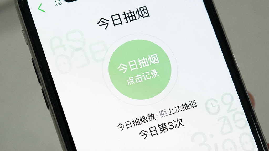 一部手机屏幕特写,画面中显示“今日抽烟”应用记录页面,页面中央有一个醒目的圆形记录按钮,按钮下方显示今日抽烟次数和距上次抽烟的时间,界面配色以白色和浅绿色为主,风格清爽,布局简洁,画质干净,无多余元素,文字为中文“今日抽烟”“点击记录”“今日第3次”