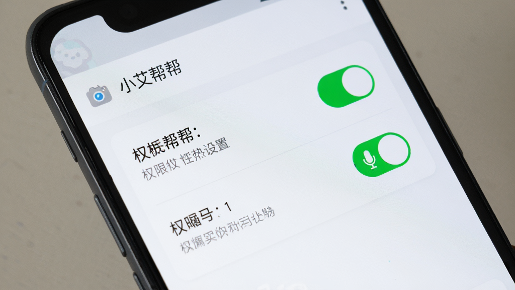 画面主体是一部安卓手机,屏幕上显示“小艾帮帮”软件的权限设置页面,摄像头和麦克风权限开关处于开启状态。布局为手机正面特写,背景简洁。排版清晰,风格写实。细节包括权限开关的绿色状态、清晰的文字说明、手机边框。画质高清,画面干净,无多余元素。
