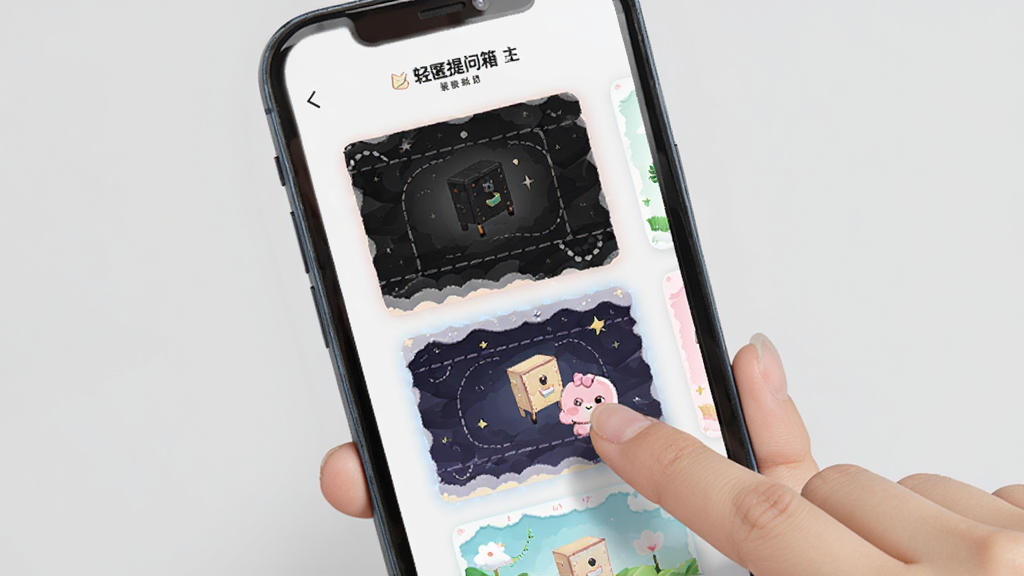 手机屏幕展示“轻匿提问箱”的主题装扮设置页面,屏幕中显示多种不同风格的主题缩略图,包括粉色可爱风、深色暗黑风、绿色清新风等,用户正在点击其中一个主题进行预览,背景为浅灰色,画面明亮清晰,风格活泼