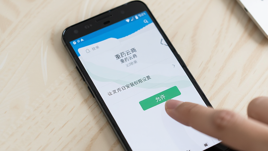 一部安卓手机放置在桌面上,屏幕显示“重药云商”APP的安装权限设置页面,旁边有手指点击“允许”按钮的动作,背景为浅色桌面,风格写实,画质清晰,干净,无多余元素