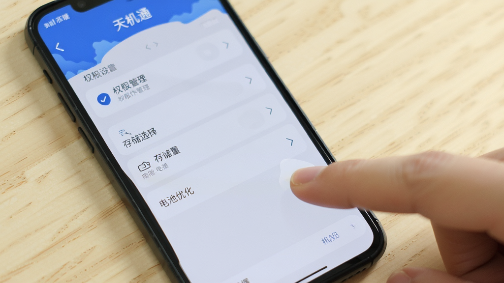一部手机屏幕显示“天机通”设置界面,界面中有权限管理、存储选择、电池优化等选项,手机旁边有手指点击屏幕的示意,背景为浅色桌面,风格简洁明了,画质清晰,干净无多余元素。