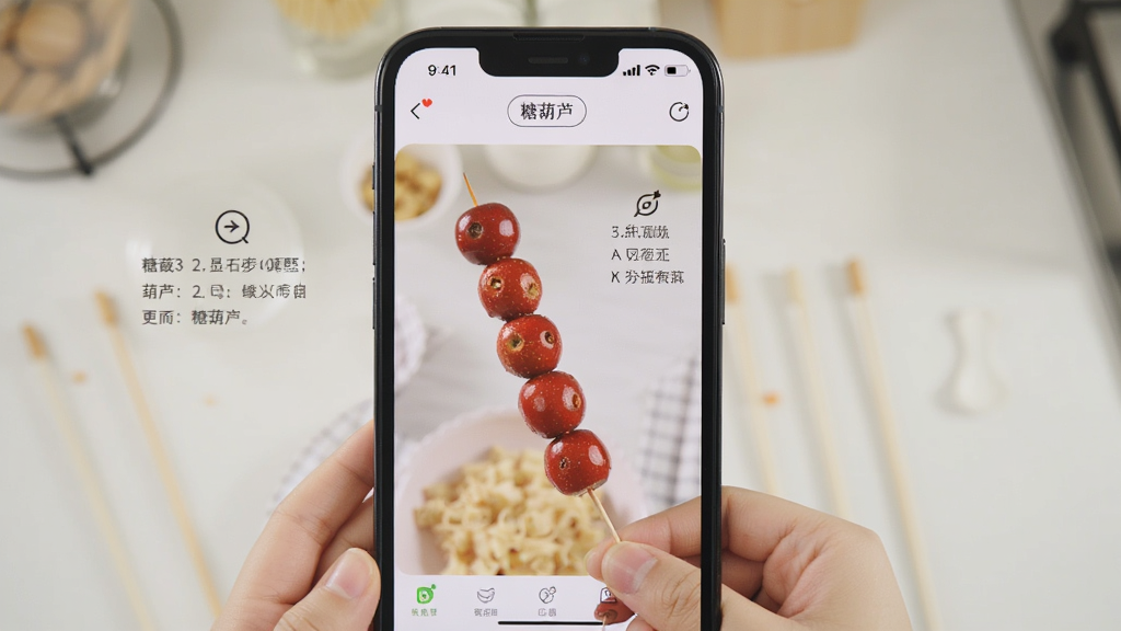 一个手机屏幕显示糖葫芦应用中的视频教程页面,画面中有一双手正在将山楂串成串,旁边有文字步骤提示,背景为厨房操作台,风格写实明亮,画质清晰,干净无多余元素