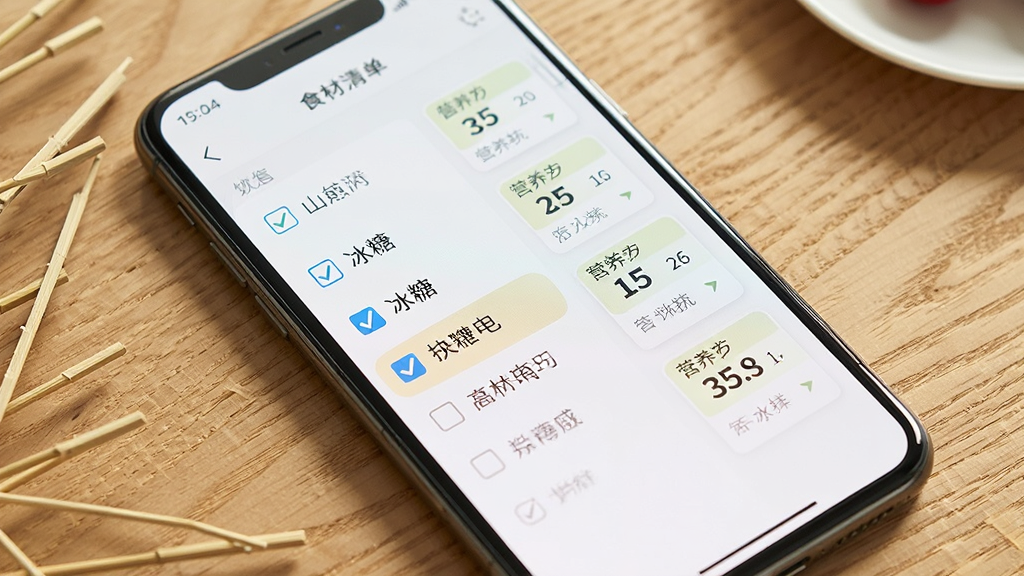一张手机屏幕显示糖葫芦应用食材清单页面的图片,清单上有山楂、冰糖、竹签等条目,旁边有勾选框和营养数据小卡片,背景为木质桌面,风格清新自然,画质清晰,干净无多余元素
