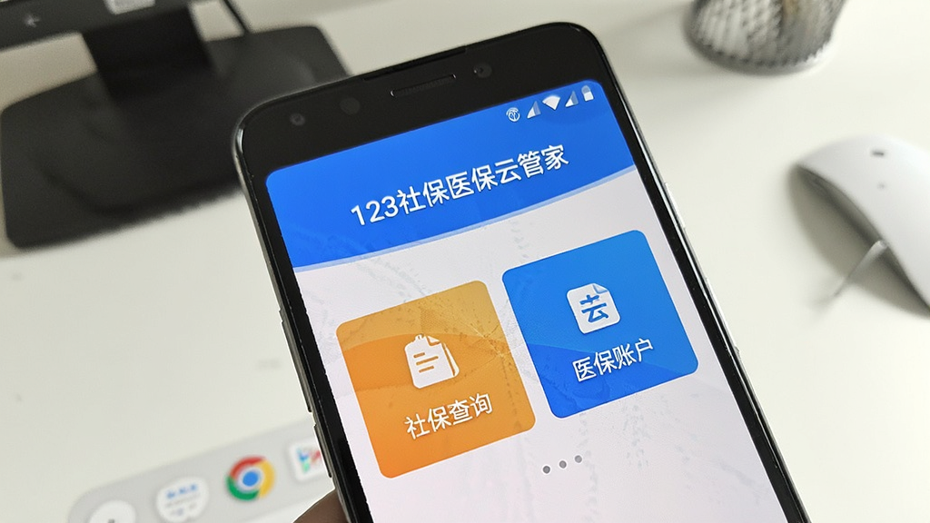 一张展示123社保医保云管家在安卓手机上安装完成并打开运行的实拍风格图片,画面中手机屏幕显示应用主界面,界面顶部有“123社保医保云管家”文字标识,中部展示社保查询和医保账户两个主要功能入口,手机周围有简洁的桌面背景,整体光线明亮,画质清晰,风格真实自然,无多余元素
