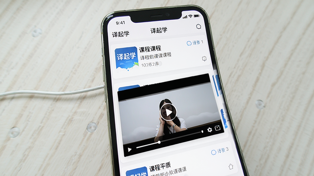 一张展示译起学课程学习界面的图片,主体为手机屏幕显示课程列表与视频播放窗口,布局为纵向滚动式,排版整齐,风格为教育类应用常见的清爽风格,细节包括课程封面图、进度条和“译起学”应用名称,画质高清,画面干净,无多余元素