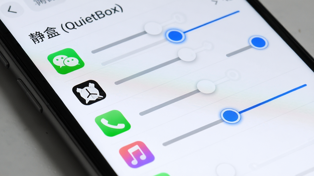 一部手机屏幕特写,显示“静盒 (QuietBox)”的应用音量管理列表,列表中排列着微信、闹钟、电话、音乐等应用图标,每个图标右侧有独立的音量滑块,布局为纵向列表排版,风格为极简浅色UI,细节包括清晰的图标、滑块轨道为浅灰色、选中状态为蓝色高亮,画质高清,干净无多余元素