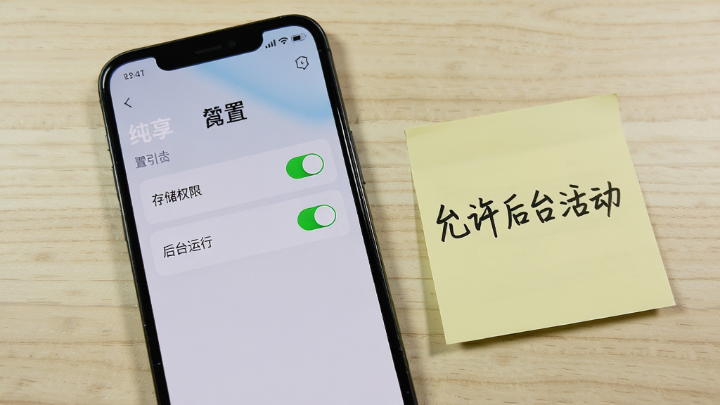 一部手机屏幕显示纯享的权限设置引导页面,页面上有存储权限与后台运行两个开关项,手机旁边放着一张写有“允许后台活动”的便签纸,背景为浅色桌面,风格实用教程感,细节上突出开关按钮与便签文字,画质清晰,干净,无多余元素