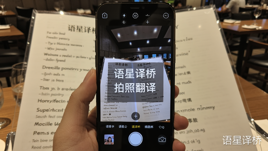 展示语星译桥拍照翻译功能的预览图,手机摄像头对准一份英文菜单,屏幕上实时叠加显示中文翻译内容,画面清晰,字体醒目,背景为餐厅环境,画质干净,无多余元素,带有“语星译桥”水印。