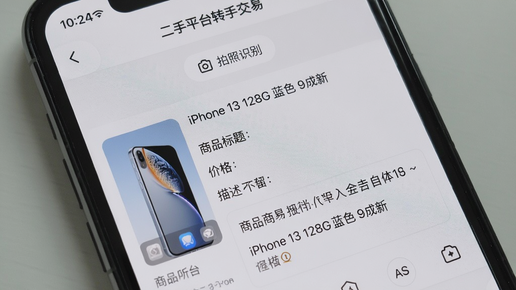 主体为一部手机屏幕,屏幕中显示“二手平台转手交易”发布商品页面,页面顶部有“拍照识别”按钮,下方自动识别出“iPhone 13 128G 蓝色 9成新”,并自动填入商品标题、价格、描述等字段,背景为浅灰色,排版简洁,风格清爽,细节丰富,画质清晰,干净,无多余元素