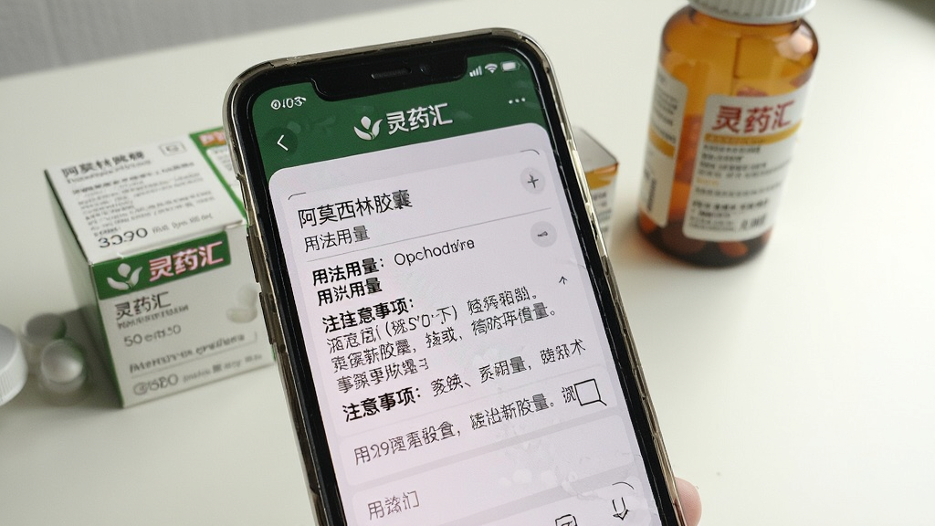 一张手机扫描药品包装盒的实拍图,手机屏幕显示“灵药汇”药品识别结果页面,上面有药品名称“阿莫西林胶囊”、用法用量、注意事项,背景为白色桌面,旁边摆放药盒和药瓶,自然光线下拍摄,画面清晰,对焦准确,无多余杂物,高分辨率