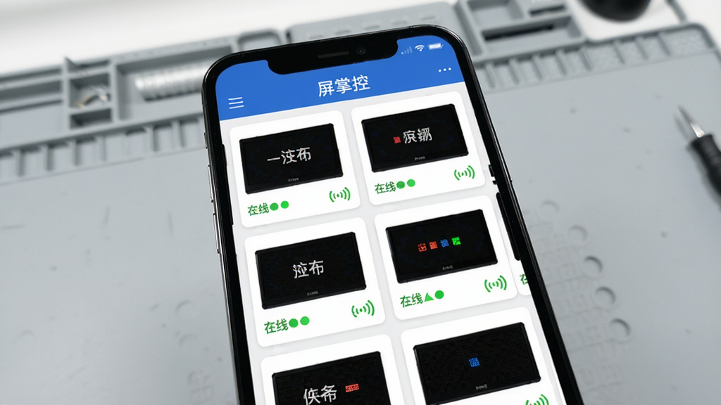 手机屏幕展示屏掌控APP的设备列表界面,顶部有“屏掌控”标题栏,下方排列多个LED屏幕卡片,每个卡片显示屏幕名称、在线状态和信号图标,背景为浅灰色工作台,风格简洁清晰,细节丰富,画质干净无多余元素
