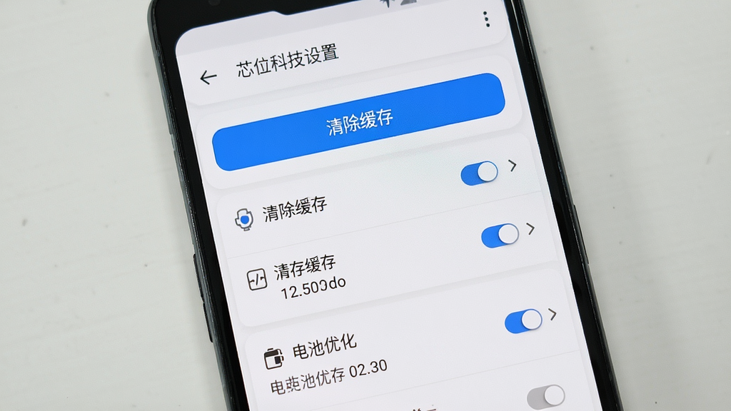 画面主体为一部竖屏安卓手机,屏幕中显示芯位科技设置界面,包含清除缓存按钮与电池优化选项;布局采用上下结构,顶部为标题,中部为功能列表;排版清晰,重点按钮用蓝色高亮;风格为简约工具风,白底灰字;细节包含开关控件、箭头指示、缓存大小数值;画质高清,画面干净,无多余元素。