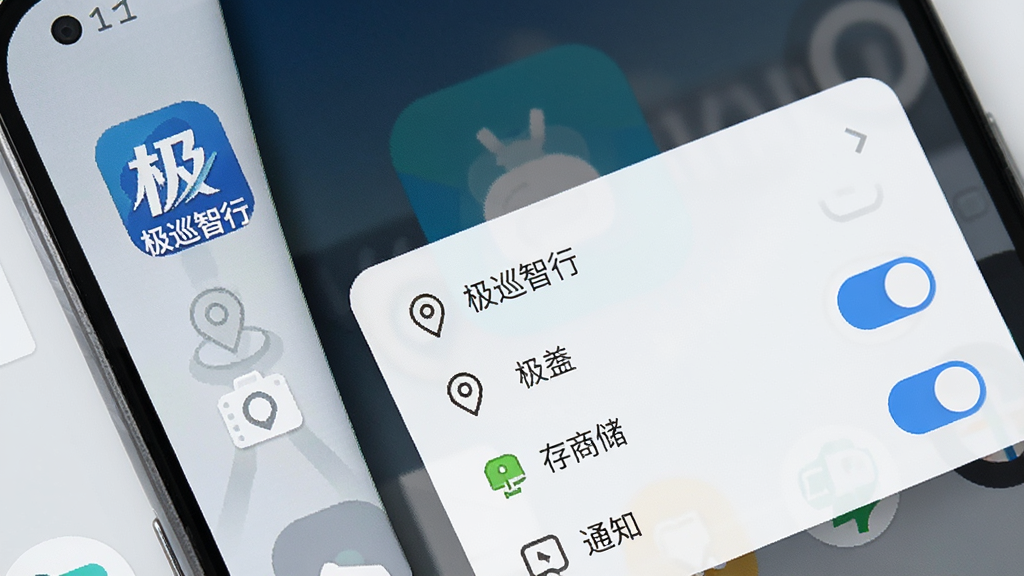 一张安卓手机桌面局部特写图,手机屏幕上显示“极巡智行”应用图标与权限设置弹窗,旁边有定位、存储、通知三个权限开关示意,背景为浅灰色桌面,整体风格简洁清晰,画质干净,无多余元素