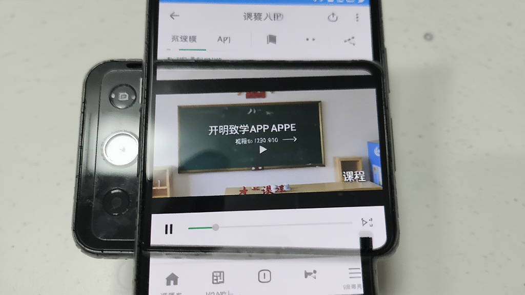 一部安卓手机展示开明致学APP的视频播放界面,主体为手机屏幕上的课程视频和下方进度条,布局为竖屏手机正面展示,风格为真实使用场景摄影风,细节包括手机边框和屏幕反光效果,画质清晰,干净,无多余元素