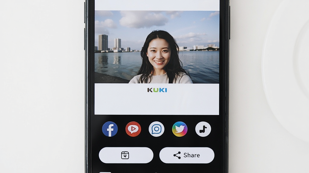 KUKI相机分享界面,手机屏幕显示照片预览和多个社交平台图标,底部有保存和分享按钮,背景为白色,风格简约,画质清晰,无多余元素