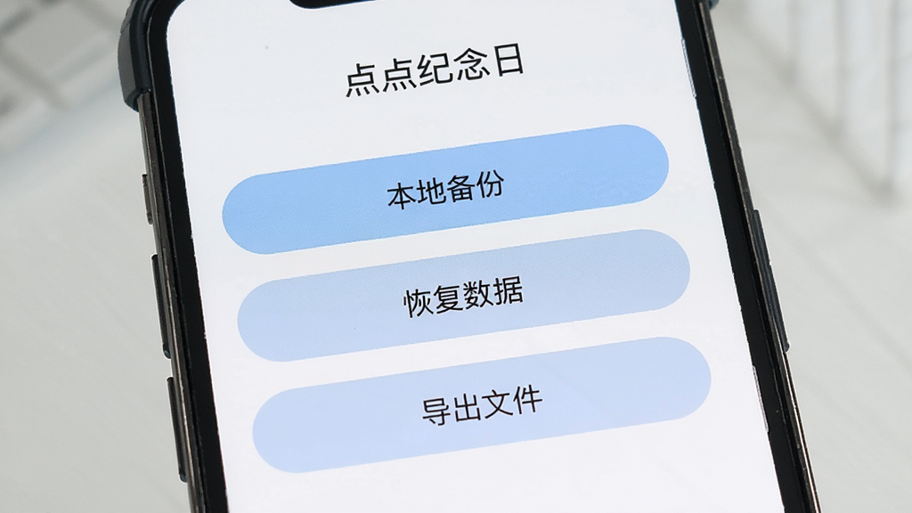 一张展示“点点纪念日”数据备份设置界面的图片,手机屏幕上显示“本地备份”“恢复数据”“导出文件”三个选项按钮,界面采用浅色主题,按钮为圆角矩形,背景干净,画质清晰,风格简洁商务,无多余干扰元素