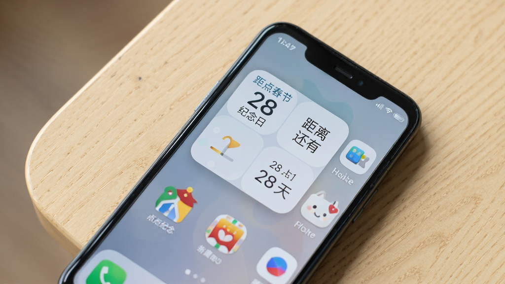一部安卓手机平放在浅色木质桌面上,手机桌面显示着“点点纪念日”的2x2方形小组件,小组件内清晰显示“距离春节还有 28 天”字样,旁边还有几个应用图标,画面采用俯拍角度,光线柔和自然,风格干净写实,画质细腻,无多余元素