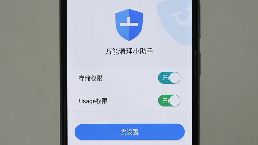 一部安卓手机屏幕展示万能清理小助手的权限设置引导页面,页面中央有一个盾牌图标,下方列出存储权限和Usage权限两项,每项右侧有开启按钮,页面底部有“去设置”的蓝色按钮,背景为浅色渐变,风格简洁,画质清晰干净