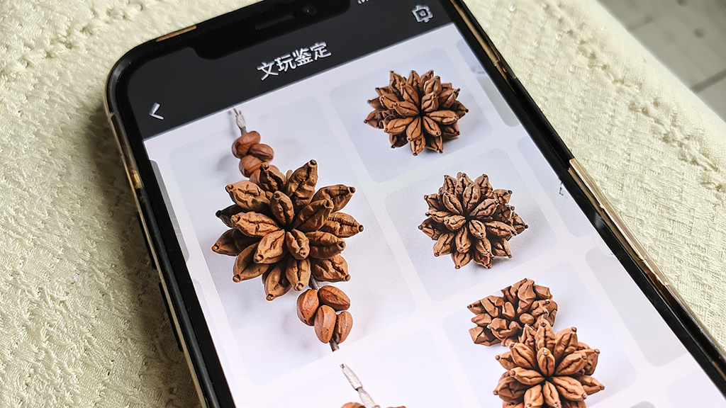 文玩鉴定App图文比对功能界面,屏幕左侧展示一串金刚菩提实拍图,右侧排列多张相似纹理的参考图,界面顶部有文玩鉴定字样,手机斜放在米白色桌布上,自然光拍摄,构图简洁,写实风格,细节丰富,画面干净,画质清晰